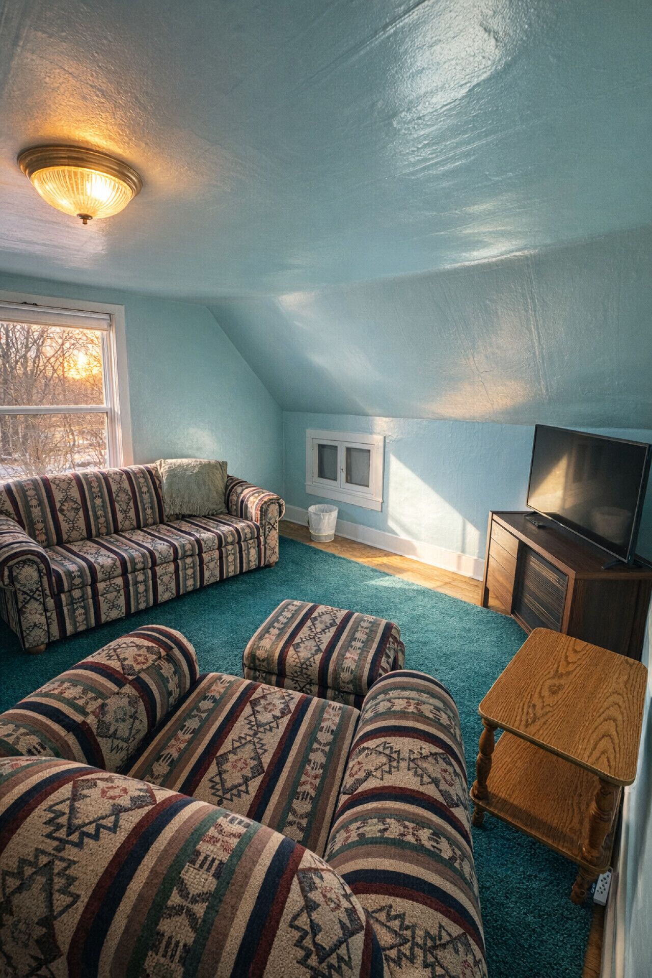 A cozy attic room with a sectional sofa, a television, and a small wooden table.