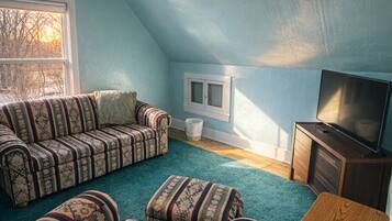 A cozy attic room with a sectional sofa, a television, and a small wooden table.