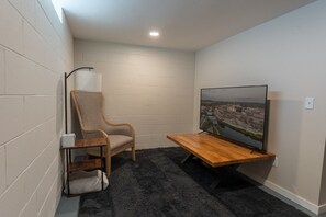 A corner room with a TV on a wooden stand, a chair, and a small table. - UWEC Campus & Clinic Retreat (Eau Claire)