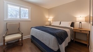 Un dormitorio con cama, mesitas de noche, una silla y una ventana.
