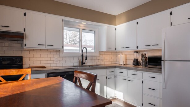Una cocina moderna con armarios blancos, una mesa de comedor de madera y un ventanal que proporciona luz natural.