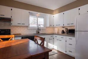 A modern kitchen with white cabinets, a wooden dining table, and a window providing natural light. - UWEC Campus & Clinic Retreat (Eau Claire)