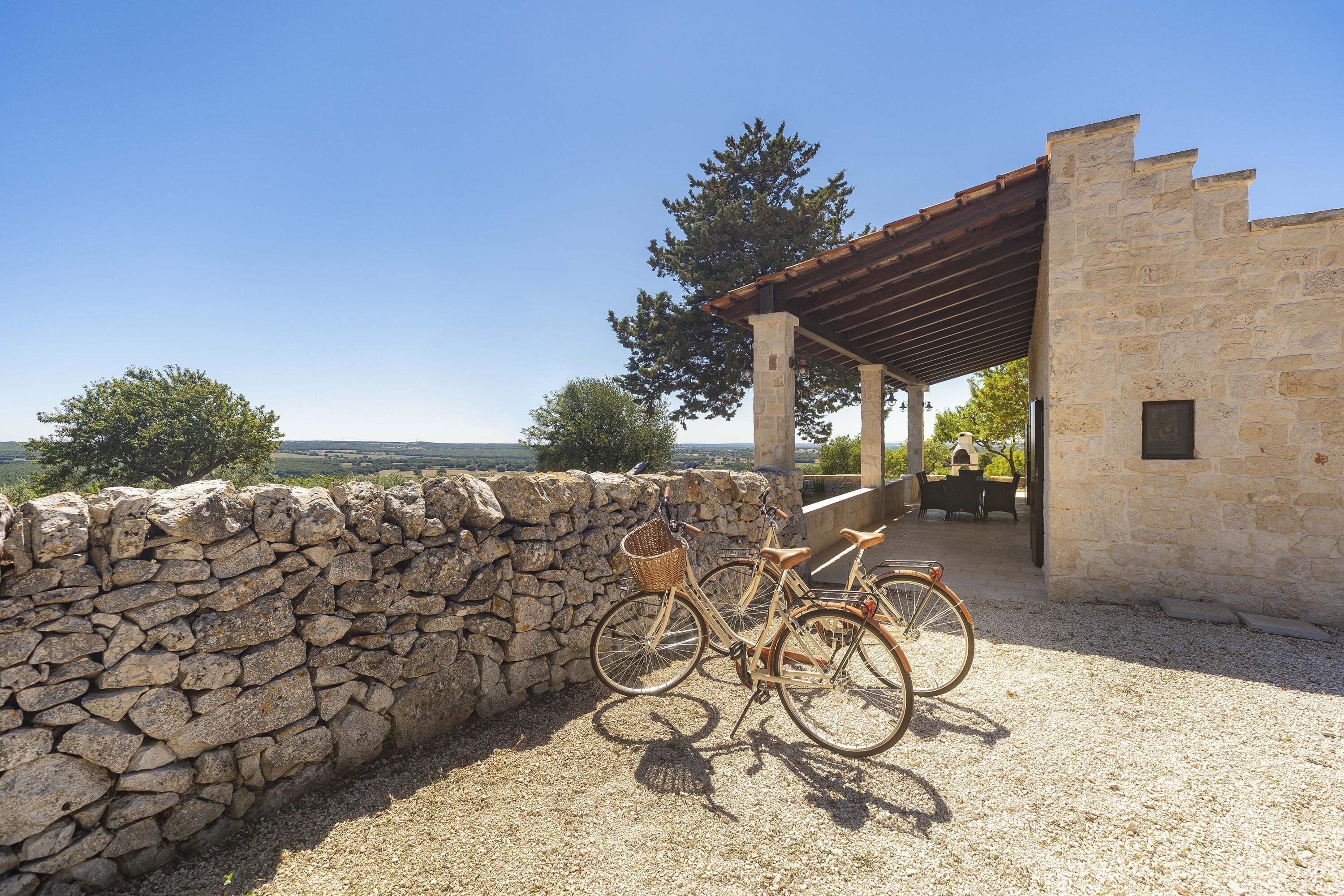 A stone wall, a bicycle, and a building with a pergola.