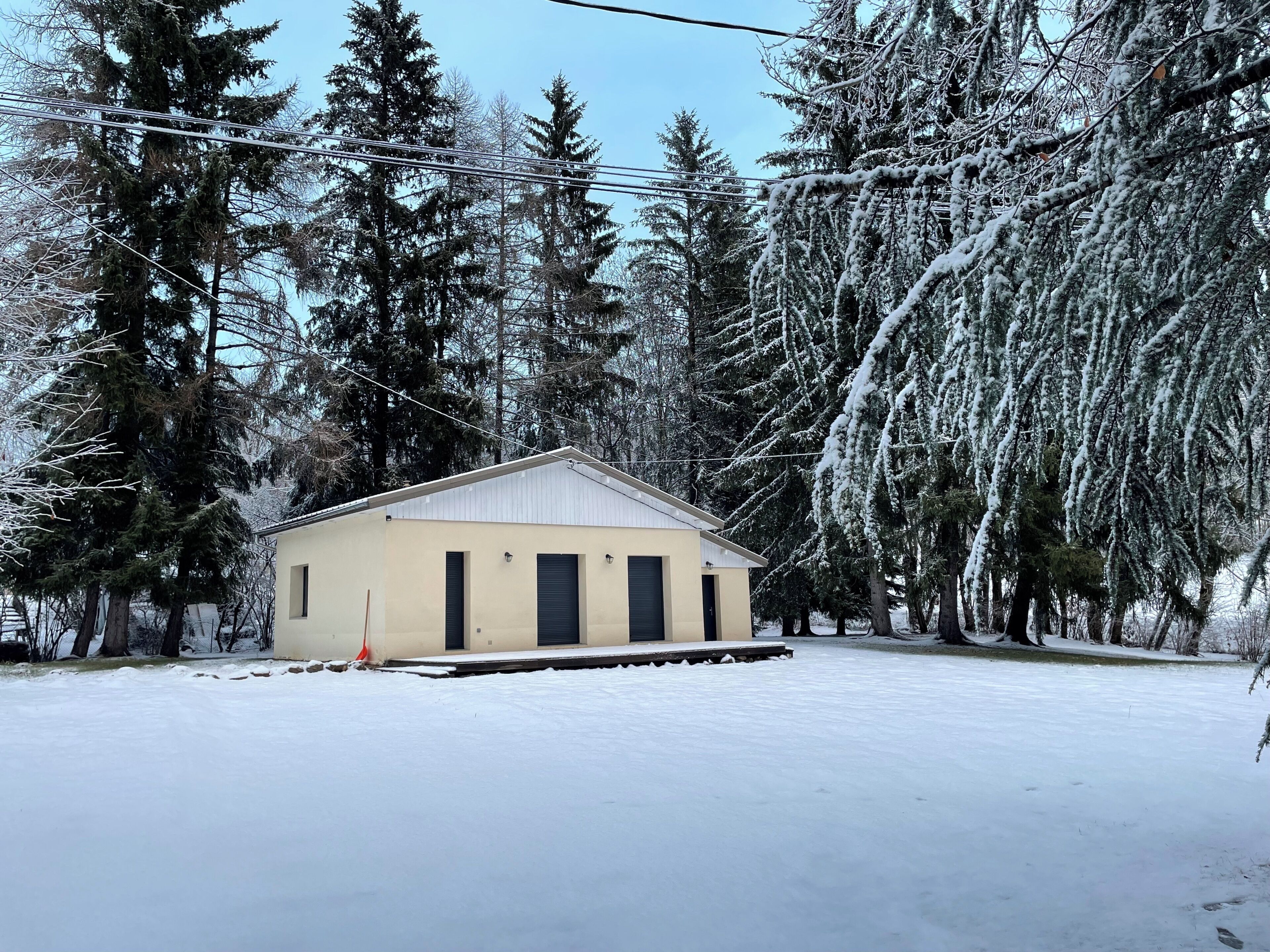 A small, single-story building with a flat roof, surrounded by snow-covered trees and a clear sky.