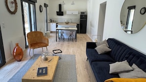 Ein modernes Wohnzimmer mit einer Couch, einem Couchtisch und einem Essbereich, im Hintergrund eine Küche.