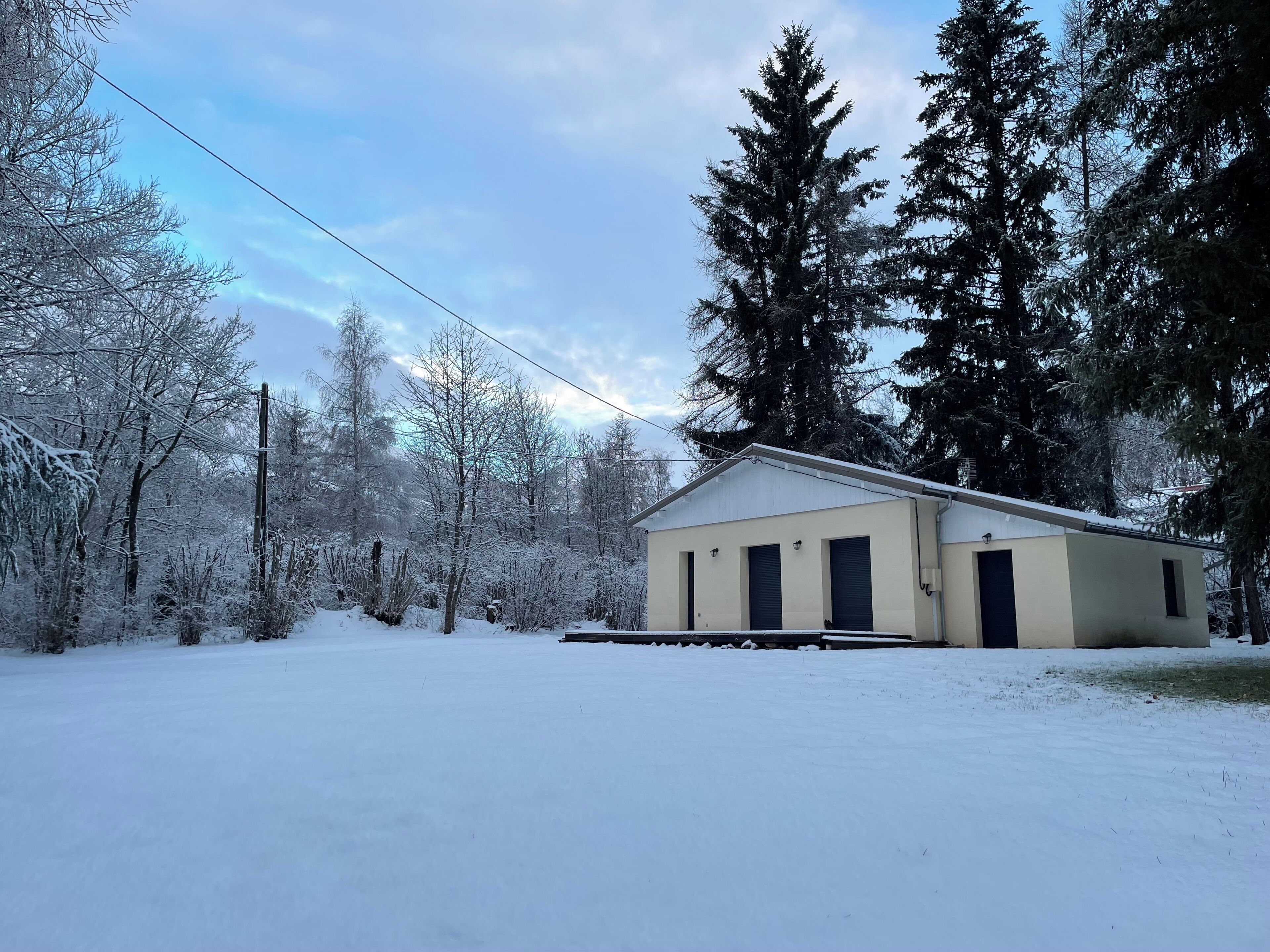 Un edificio de una sola planta con techo plano, rodeado de árboles cubiertos de nieve y un cielo despejado.