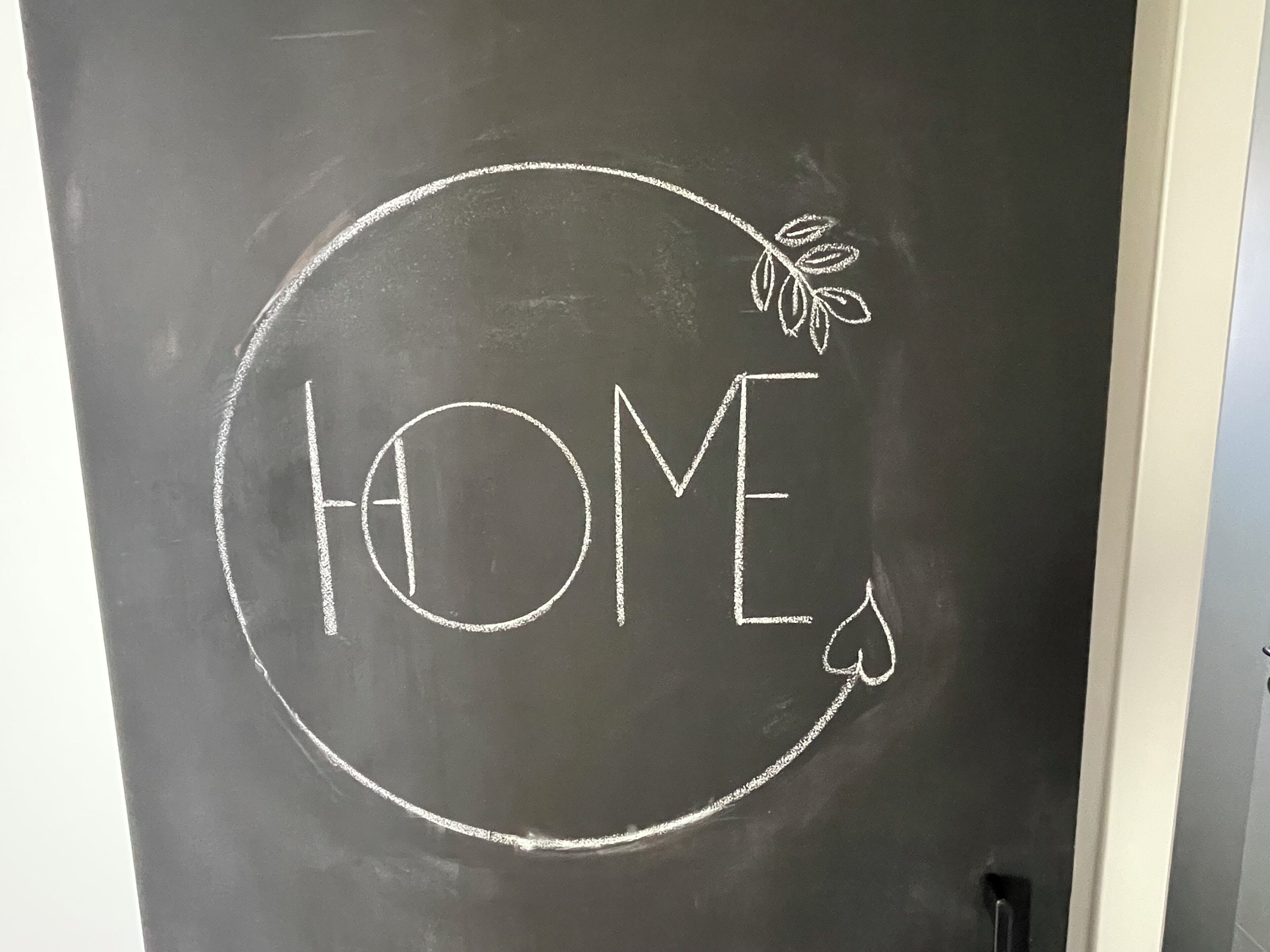 Una pizarra con la palabra 'HOME' escrita a tiza, rodeada por un círculo y un dibujo de una hoja.