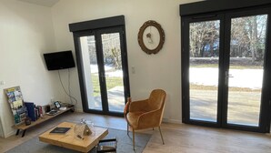 Ein Wohnzimmer mit Couchtisch aus Holz, einem braunen Sessel, einem Bücherregal und einem an der Wand montierten Fernseher.