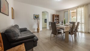 Una sala de estar moderna con un sofá de cuero negro, una mesa de comedor con sillas, un mueble de madera y un ventanal con cortinas.