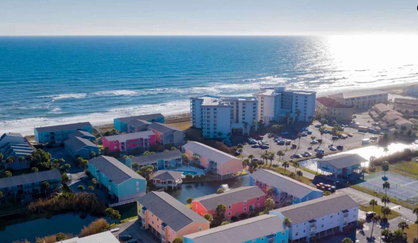 Um hotel à beira-mar com vários edifícios, uma praia e um parque de estacionamento.
