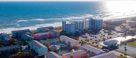 Um hotel à beira-mar com vários edifícios, uma praia e um parque de estacionamento.
