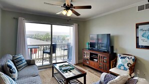 Una sala de estar con sofá, mesa de centro, televisión y un balcón con vistas.