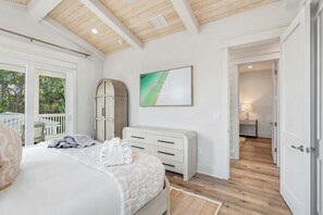 Une chambre à coucher avec un lit, une commode, un tableau et une vue sur l’extérieur.