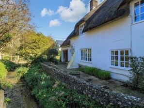 Une petite maison blanche au toit de chaume, avec un mur en pierre et un petit ruisseau.