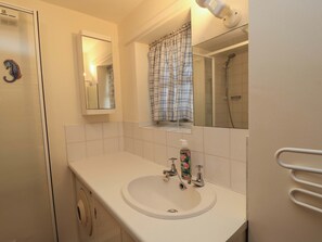 Un bany amb un lavabo, mirall, dutxa i paraula per a tovalloles.