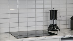 A kitchen with white tiles, a black induction cooktop, and a stainless steel range hood.