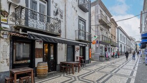 A cobblestone street with outdoor seating, a bar, and a building with a balcony.