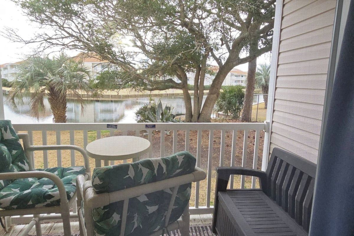 A balcony with outdoor furniture, a view of a body of water, and a building in the background.