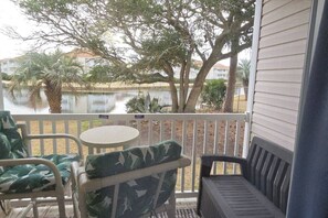 Un balcon avec du mobilier d’extérieur, une vue sur une étendue d’eau et un bâtiment en arrière-plan.