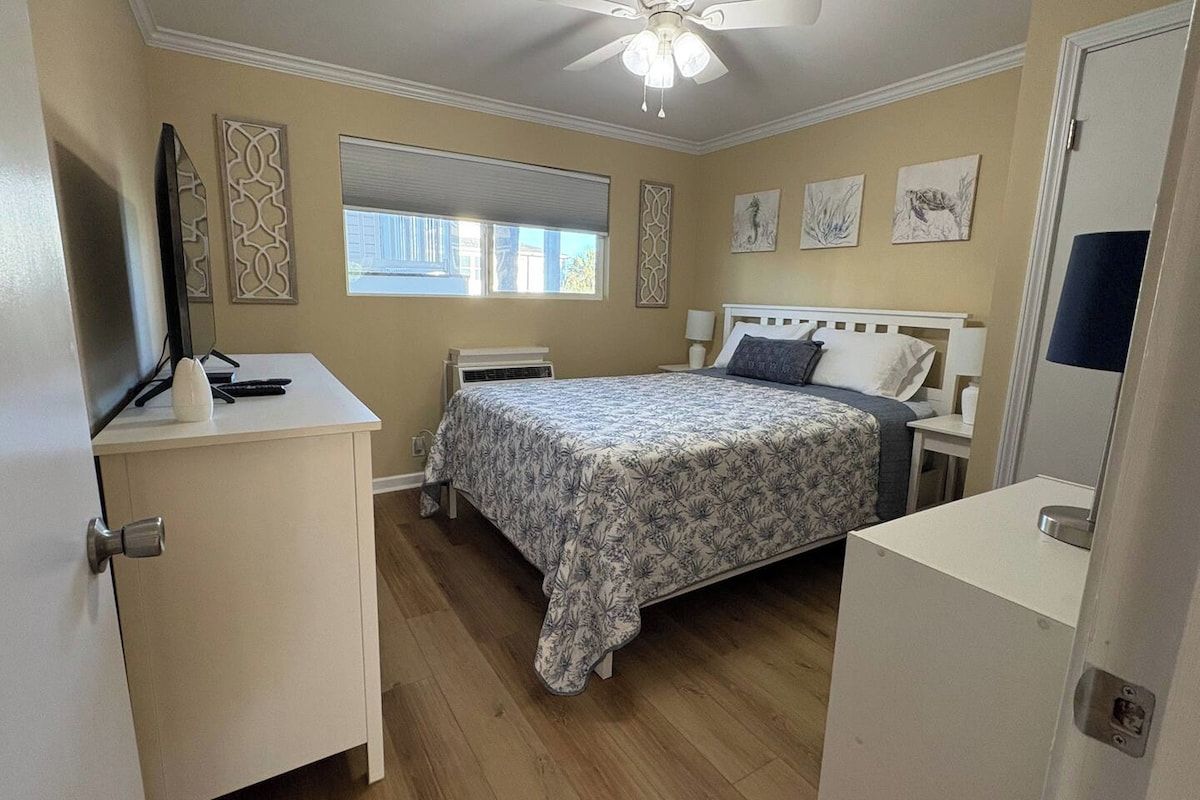A bedroom with a bed, bedside tables, a ceiling fan, and artwork on the walls.