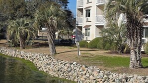 En bostadsbyggnad med en balkong, omgiven av palmer och en stenmur.