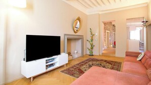 Uma sala de estar com televisão de tela plana, lareira, sofá rosa e tapete estampado.