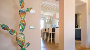 Um interior moderno com arte de parede de cactos, uma área de refeições com cadeiras e uma cozinha ao fundo.