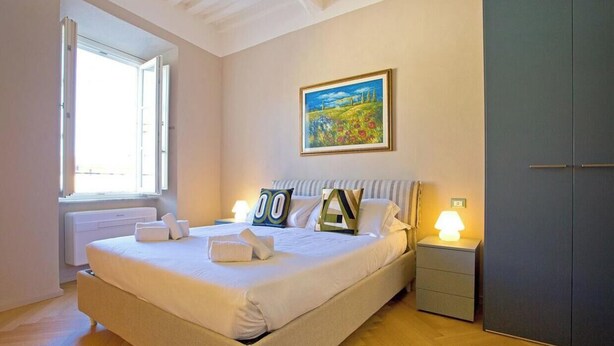 Quarto com cama, mesas de cabeceira, radiador, janela e guarda-roupa.