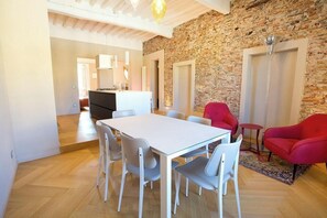 A dining area with a white table and chairs, a red armchair, and a stone wall. - Parlisium in Piazza Anfiteatro- Lucca (Lucca)