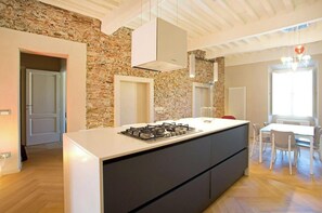 A modern kitchen with a central island, a stone wall, and a dining area with a table and chairs. - Parlisium in Piazza Anfiteatro- Lucca (Lucca)