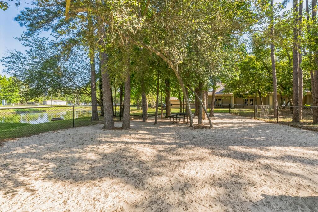 A sandy park area with trees, a fence, and a building in the background.