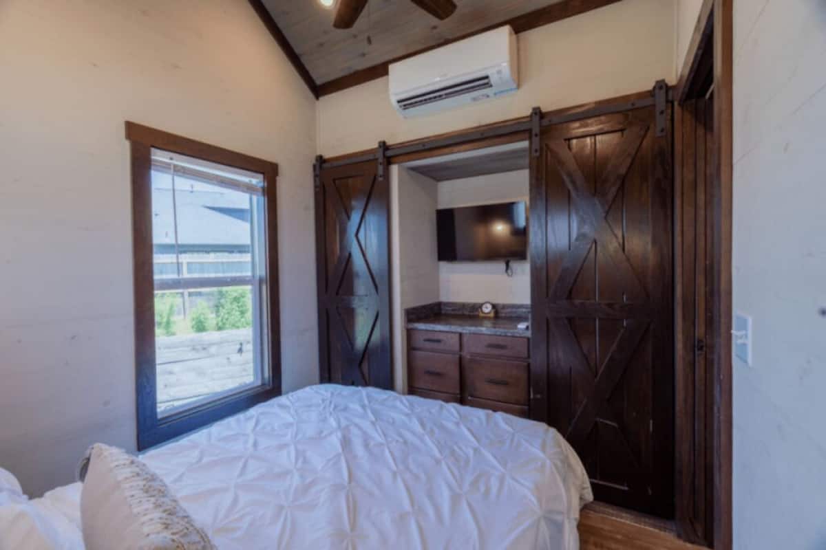 A bedroom with a bed, a window, a sliding barn door closet, and an air conditioning unit.