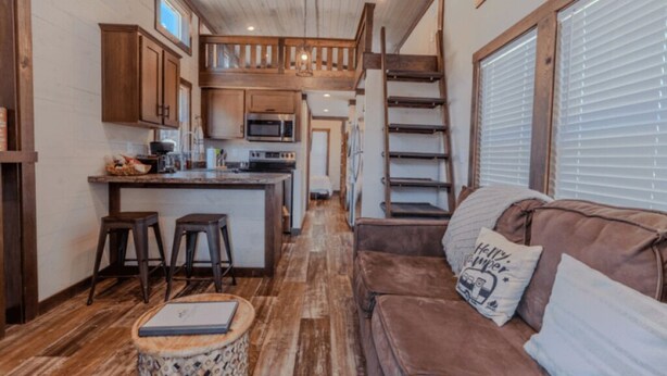 A compact kitchen with wooden cabinets, a central island, and a staircase leading to an upper level.
