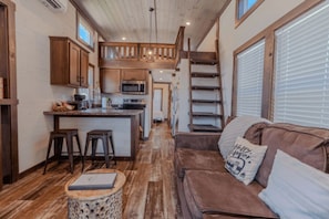 A compact kitchen with wooden cabinets, a central island, and a staircase leading to an upper level. - Rayford Crossing RV Resort (Spring)