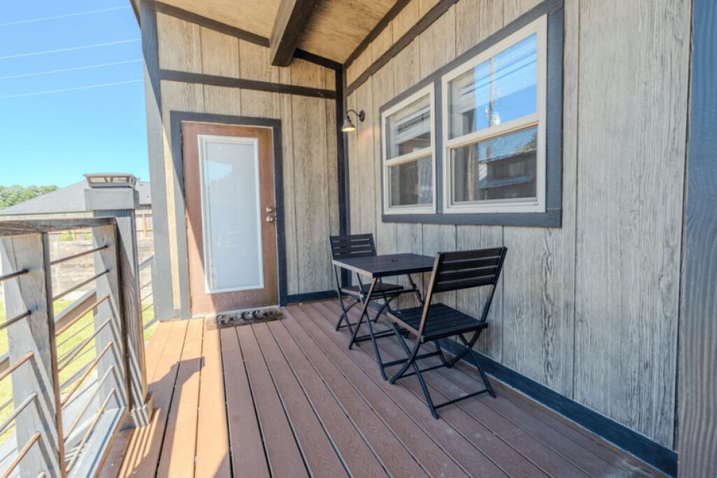 Una terraza de madera con una puerta, una ventana y una mesa con sillas.