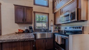 A compact kitchen with wooden cabinets, a stainless steel sink, a built-in oven, and a microwave.