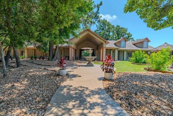 A pathway leading to a building with a central fountain, surrounded by trees and potted plants. - Rayford Crossing RV Resort (Spring)