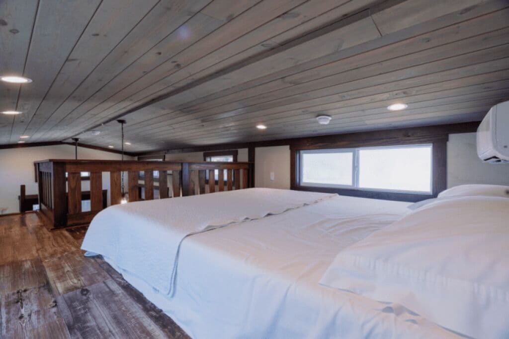 Une chambre avec un plafond en bois, un grand lit, une fenêtre et une armoire en bois.