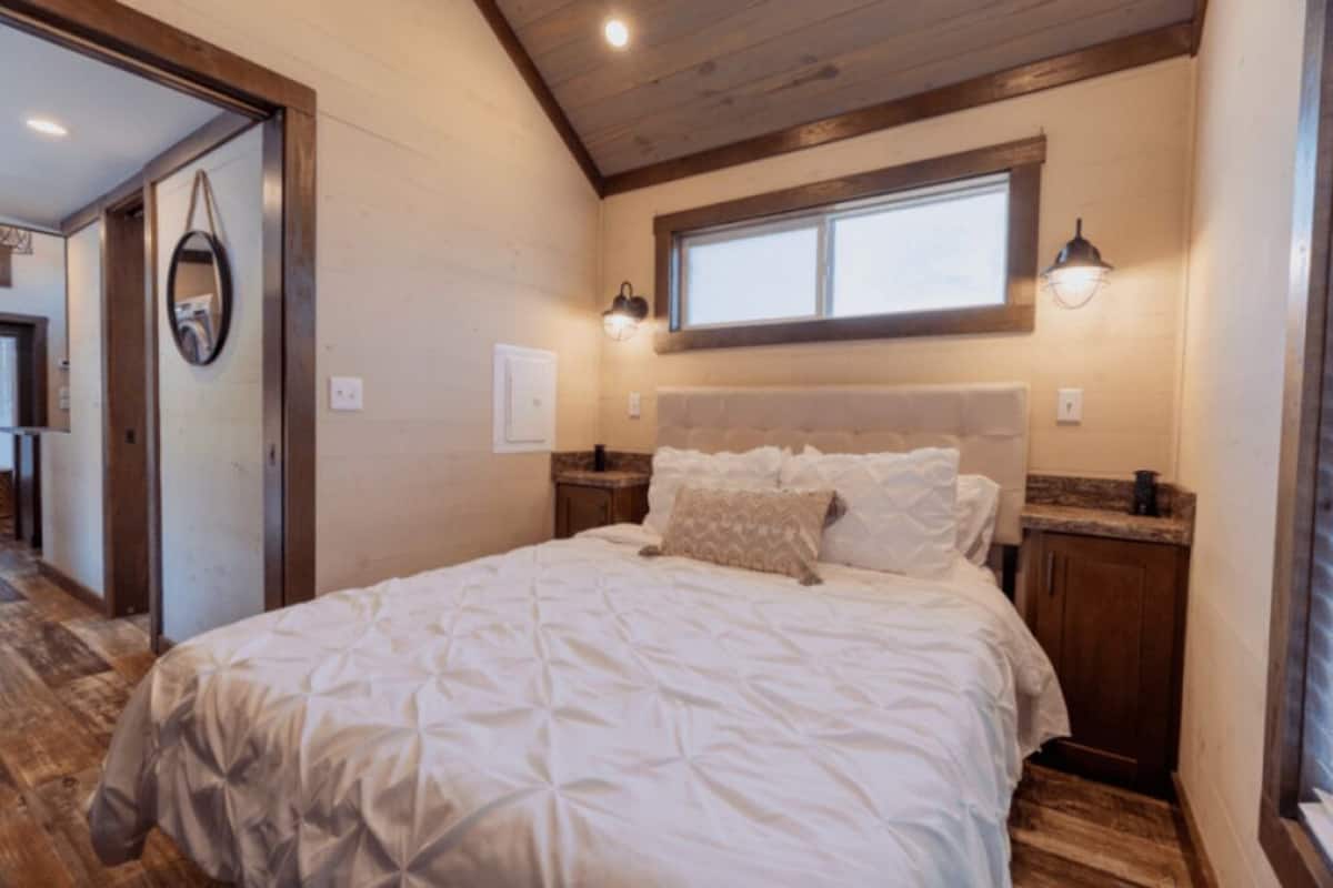 A bedroom with a large bed, wooden headboard, two bedside lamps, a window, and a door leading to another room.