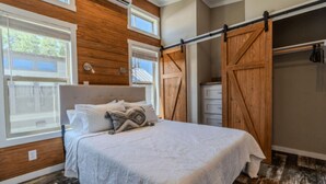 A bedroom with a bed, wooden walls, a sliding barn door closet, and a window.