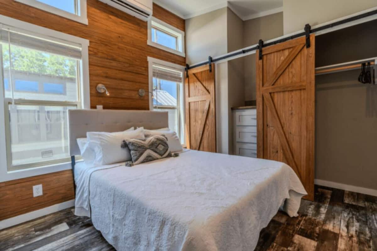 A bedroom with a bed, wooden walls, a sliding barn door closet, and a window.