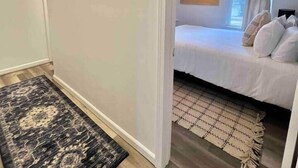Ein Schlafzimmer mit einem Bett, einem Gemälde, einem Fenster mit Vorhängen und einem gemusterten Teppich.