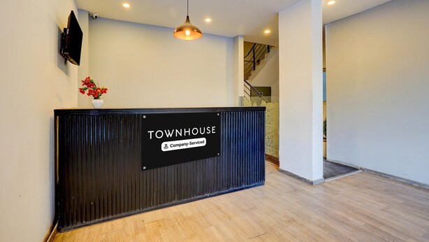 Ein Empfangsschalter mit einem Schild mit der Aufschrift 'TOWNHOUSE Company-Serviced', einem montierten Fernseher, einer Pendelleuchte und einer Treppe im Hintergrund.