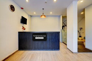 A reception desk with a sign reading 'TOWNHOUSE,' a mounted television, a clock, and a ceiling light fixture. - Townhouse Sarjapur Near Bellandur (Bengaluru)