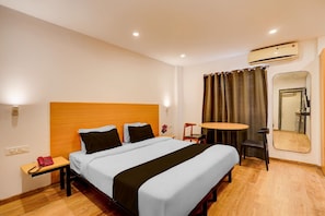 A hotel room with a bed, bedside table, chair, round table, and an air conditioning unit. - Townhouse Sarjapur Near Bellandur (Bengaluru)