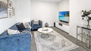 Ein modernes Wohnzimmer mit einem blauen Sofa, einem runden Couchtisch, einem Flachbildfernseher und einer dekorativen Vase.