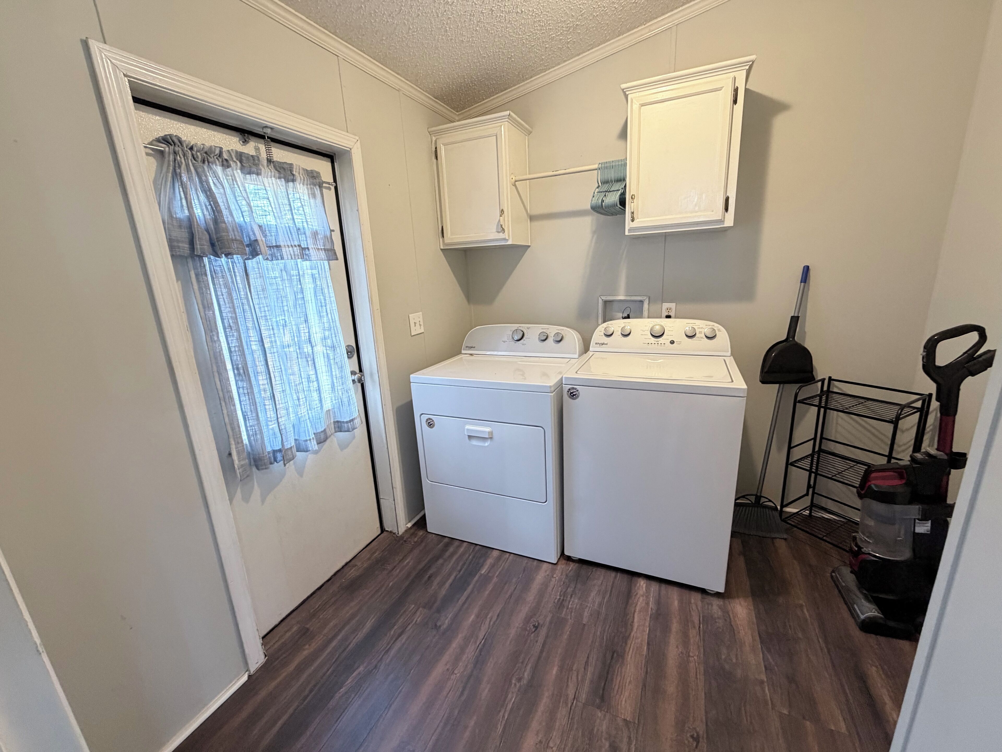 A laundry room with two white washers and dryers, a metal rack, and a vacuum cleaner.