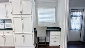 A kitchen with white cabinets, a microwave, a window with blinds, and a dark wooden floor. - Countryside Home in Beautiful Aiken SC (Aiken)