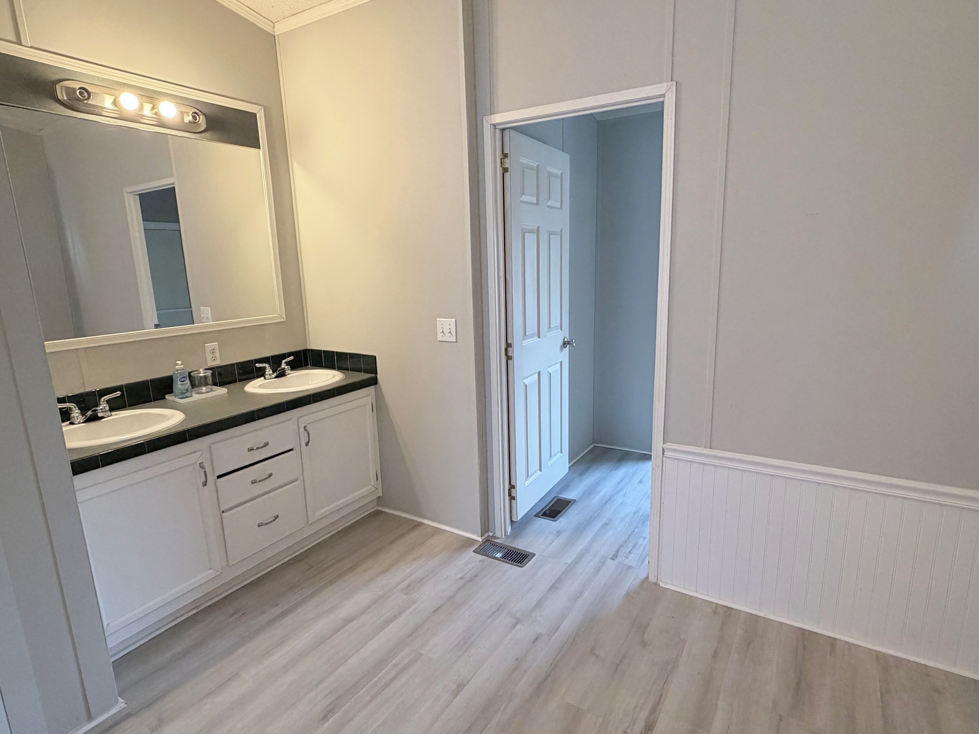 A bathroom with two sinks, a mirror, and a door leading to another room.