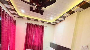 A bedroom with a bed, a ceiling fan, and red curtains. - Hotel Shyam Mahal (Khatoo)
